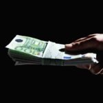 Hand überreicht ein Bündel 100-Euro-Scheine im Dunkeln – Diskussion um Abschaffung des Bargelds und Anonymität