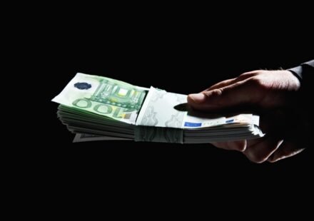 Hand überreicht ein Bündel 100-Euro-Scheine im Dunkeln – Diskussion um Abschaffung des Bargelds und Anonymität